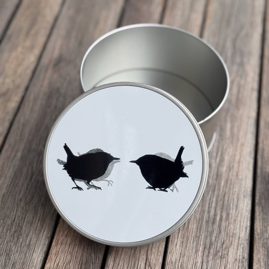 Metal tin with a white lid featuring black bird illustrations on a wooden surface