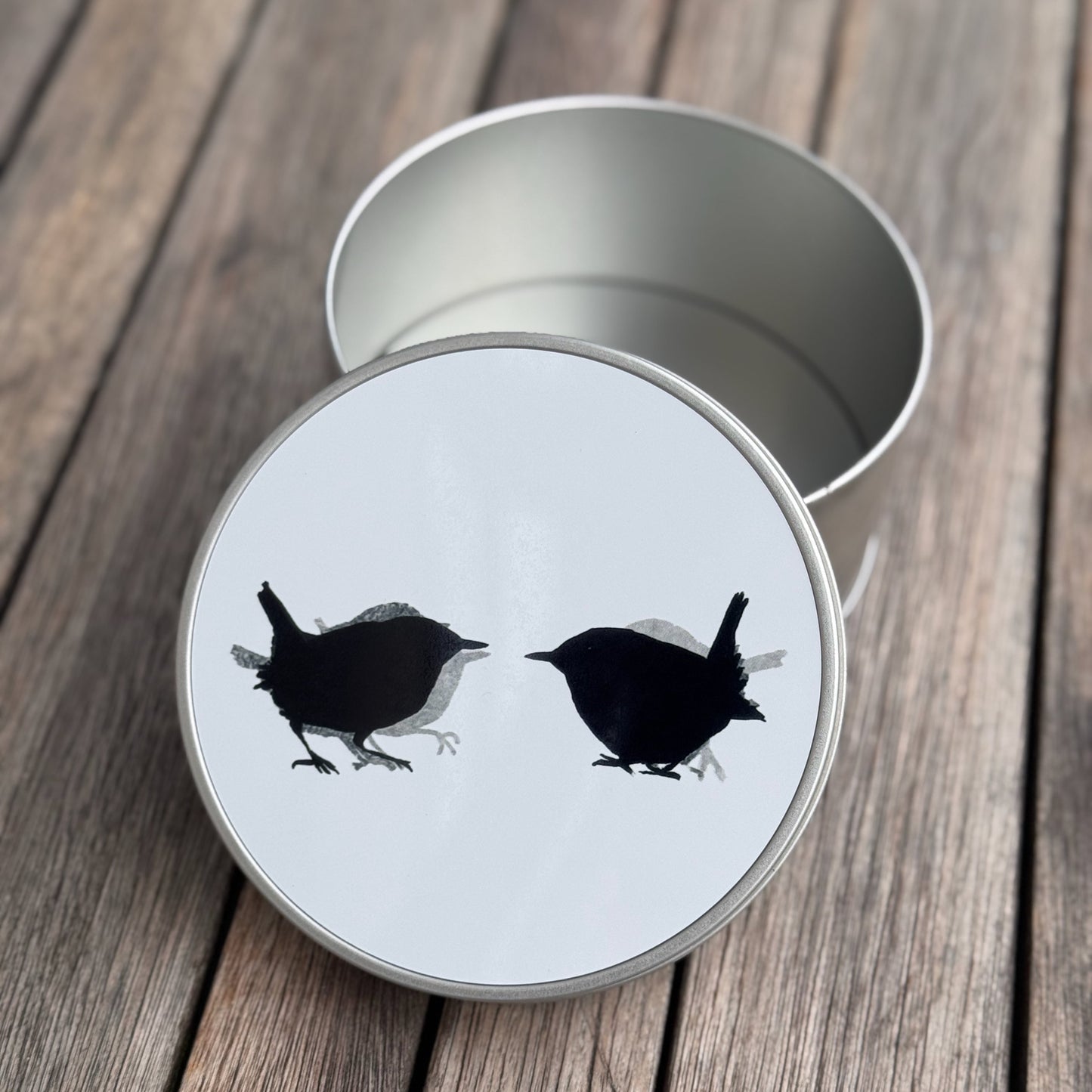Metal tin with a white lid featuring black bird illustrations on a wooden surface